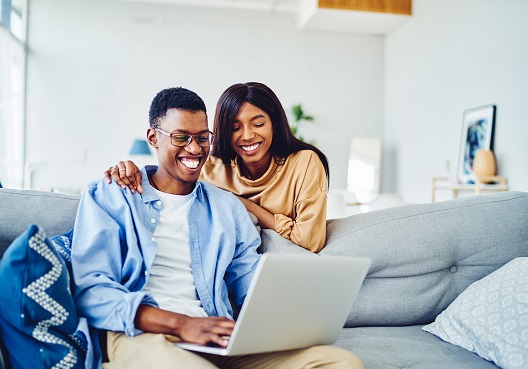 couple sitting on a couch looking at a laptop couple sitting on a couch looking at a laptop